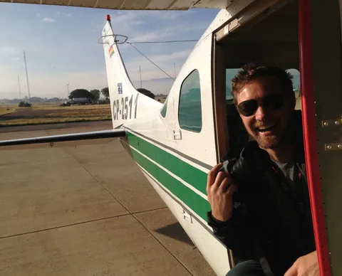 A man in sunglasses laughs at the open door of a small green and white plane.