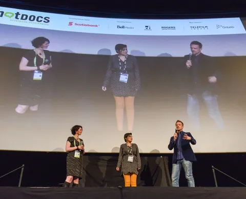 Three people speak on a stage under a large screen with the Hot Docs logo.