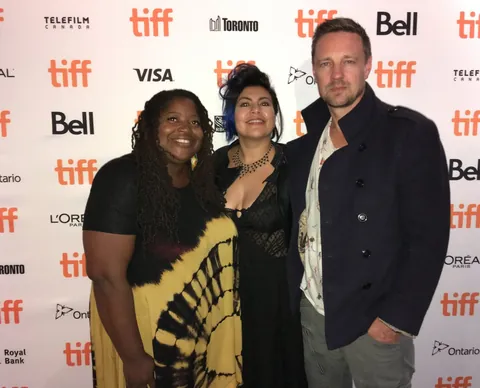 Three people pose in front of a TIFF backdrop.