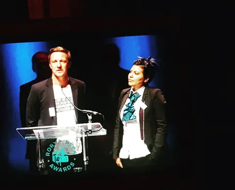 Two people stand at a lectern marked Rory Peck Awards.