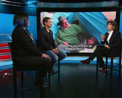 Three people sit in a television studio in front of a large screen. A CNN logo is in the corner.