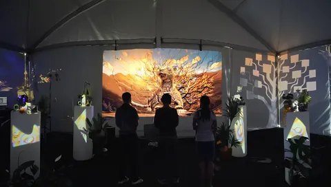 Three visitors stand before a screen showing a golden jaguar, inside a white tent with lit plinths.