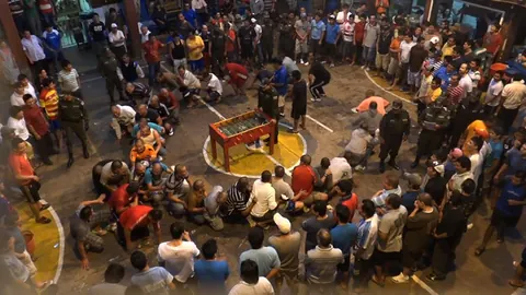 A crowd stands around a table football game in a prison courtyard, seen from above. Still from Cocaine Prison.