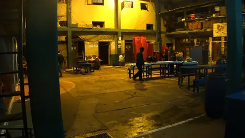 A prison courtyard at night under yellow light, its tables empty. Still from Cocaine Prison.