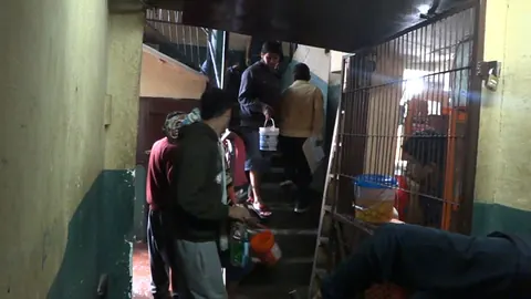 People climb a narrow stairway behind bars in a dim corridor. Still from Cocaine Prison.