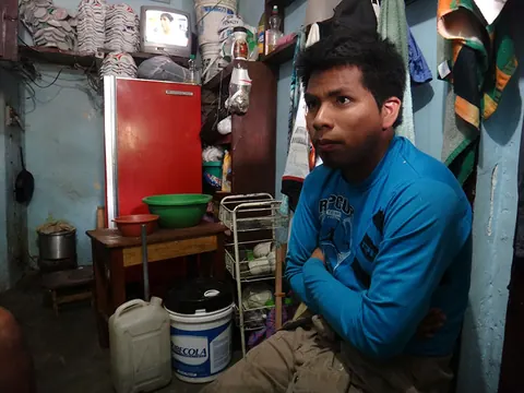 A young man in a blue top sits in a small kitchen beside a red fridge. Still from Cocaine Prison.