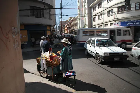 A street vendor's cart and a white car in a busy city street. Still from Cocaine Prison.