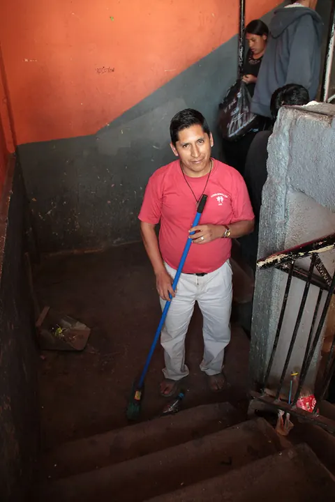 A man in a pink shirt holds a mop at the foot of a staircase. Still from Cocaine Prison.
