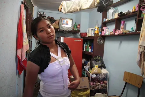 A young woman in a white top stands in a small room full of shelves. Still from Cocaine Prison.