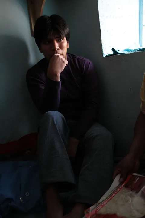 A young man sits on the floor of a dark cell, his chin on his hand. Still from Cocaine Prison.