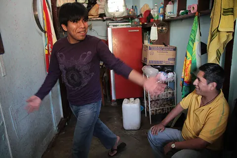 A man dances in a small room while a man in a yellow shirt sits and watches. Still from Cocaine Prison.