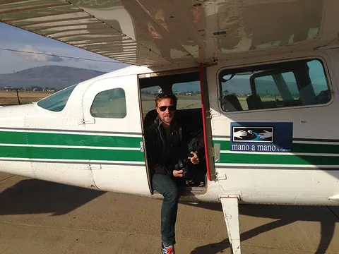 A man in sunglasses sits at the open door of a small green and white plane. Still from Cocaine Prison.