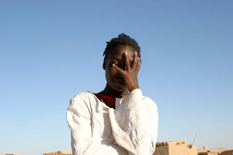 A young man covers part of his face with his hand, under a blue sky. Still from Stolen.