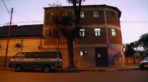 A round brick building at dusk, with a van parked in front. Still from The Bolivian Case.