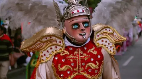 A dancer in a carnival costume, with a mask and white feathered wings. Still from The Bolivian Case.