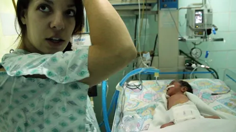 A young woman in a hospital gown stands beside a baby in an incubator. Still from The Bolivian Case.