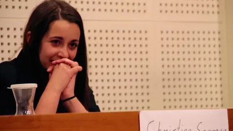 A young woman sits at a courtroom table, her hands clasped. Still from The Bolivian Case.