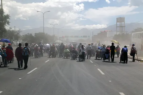 Marchers in wheelchairs and on foot fill a wide road under a dusty sky. Still from The Fight.