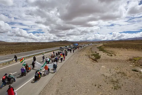 A long line of marchers in wheelchairs moves along a highway across the altiplano. Still from The Fight.