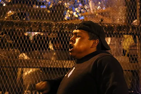A man shouts through a wire fence at night. Still from The Fight.