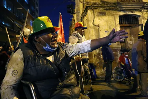 A man in a wheelchair and a hard hat shouts and stretches out his arm in a street at night. Still from The Fight.