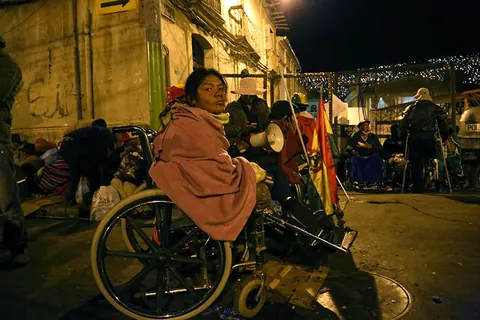 A woman in a wheelchair, wrapped in a pink blanket, waits in a street at night. Still from The Fight.