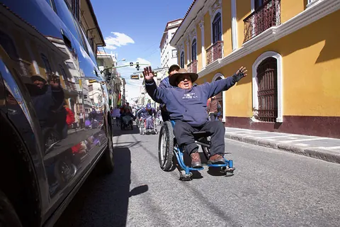 A man in a wheelchair raises his arms in a sunny street. Still from The Fight.