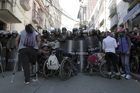 Police with shields block a street where protesters in wheelchairs wait. Still from The Fight.