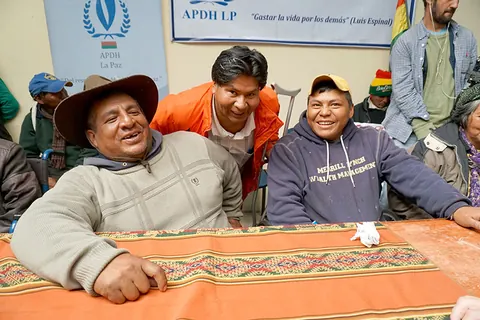 Three men smile at a table covered with a woven cloth. Still from The Fight.