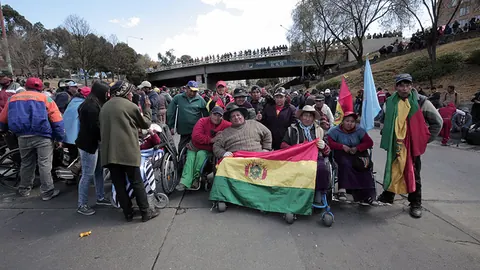 Protesters gather behind a large Bolivian flag on a road below a bridge. Still from The Fight.