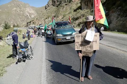 A woman holds a cardboard sign on a mountain road as marchers pass. Still from The Fight.