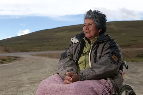 A woman wrapped in a pink blanket sits in a wheelchair on a hillside. Still from The Fight.