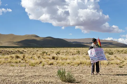 A person holds a Bolivian flag alone on a dry plain under a big sky. Still from The Fight.