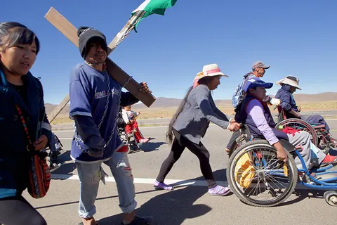 Marchers walk with a cross and wheelchairs along a highway. Still from The Fight.