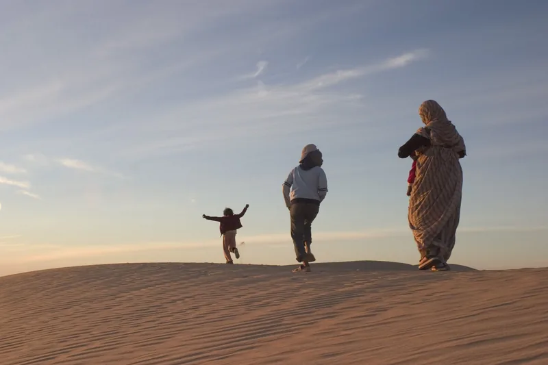 Three figures walk along the crest of a sand dune.