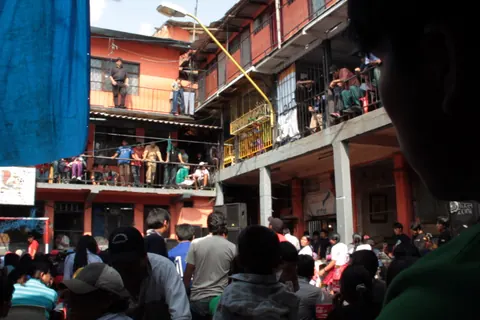 Crowds fill the walkways and the courtyard of a prison block several storeys high. From Prison X.